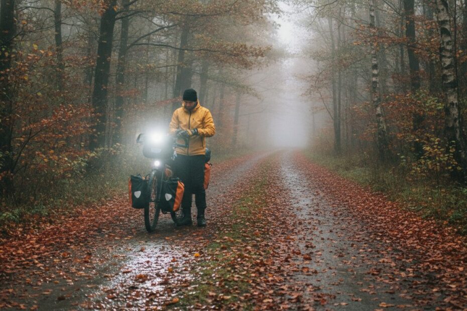 Rowerzysta z rowerem wyprawowym z sakwami i lampą na mokrej leśnej drodze jesienią